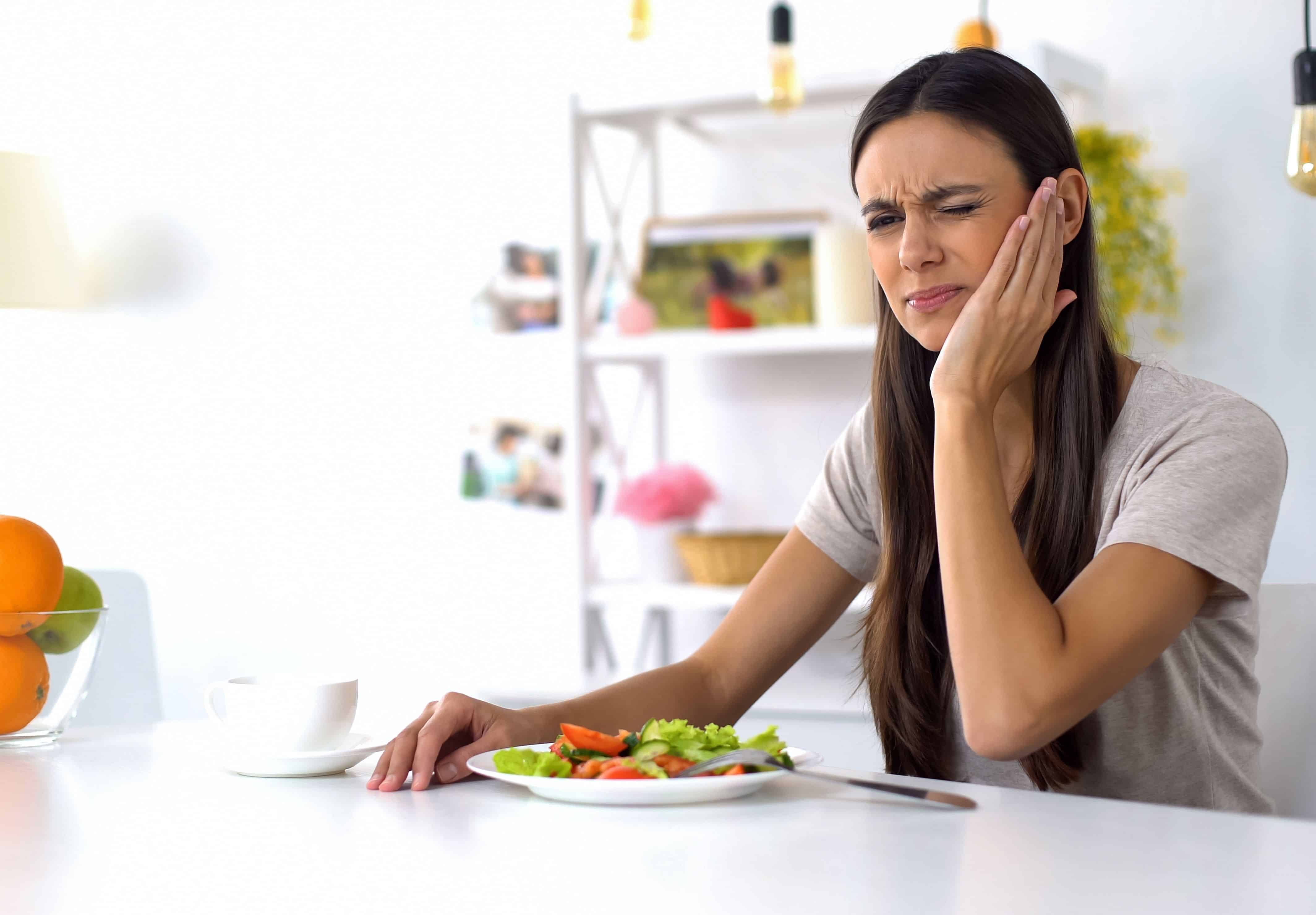 woman eating salad feeling tooth ache