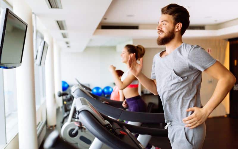 man and woman running on treadmills in gym doing cardio workout
