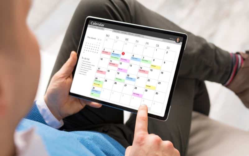 A man is utilizing a calendar application on his tablet to manage and keep track of his schedule.