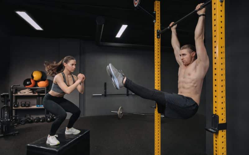 Handsome shirtless muscular man doing abdominal exercise while fit sporty woman doing box jump exercise
