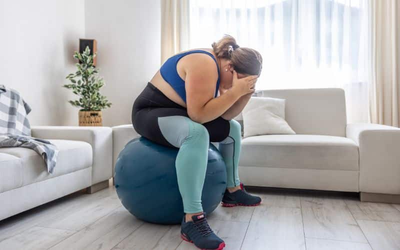Frustrated obese woman sitting on a swiss ball and crying because of her overweight